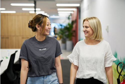 Two woman walking down a hallway, smiling